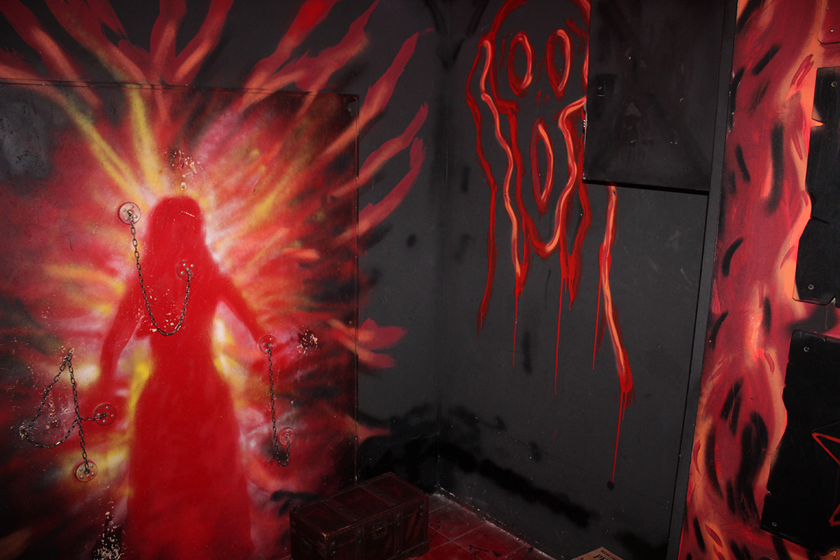 Une silhouette peinte et des cha&icirc;nes sur un mur rouge et noir, salle Haunted Room à La D&eacute;fense