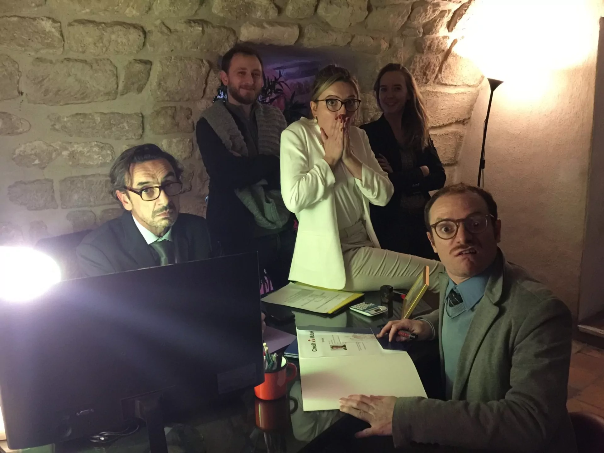Des comédiens et des joueurs autour d'un bureau, dans une cave voûtée