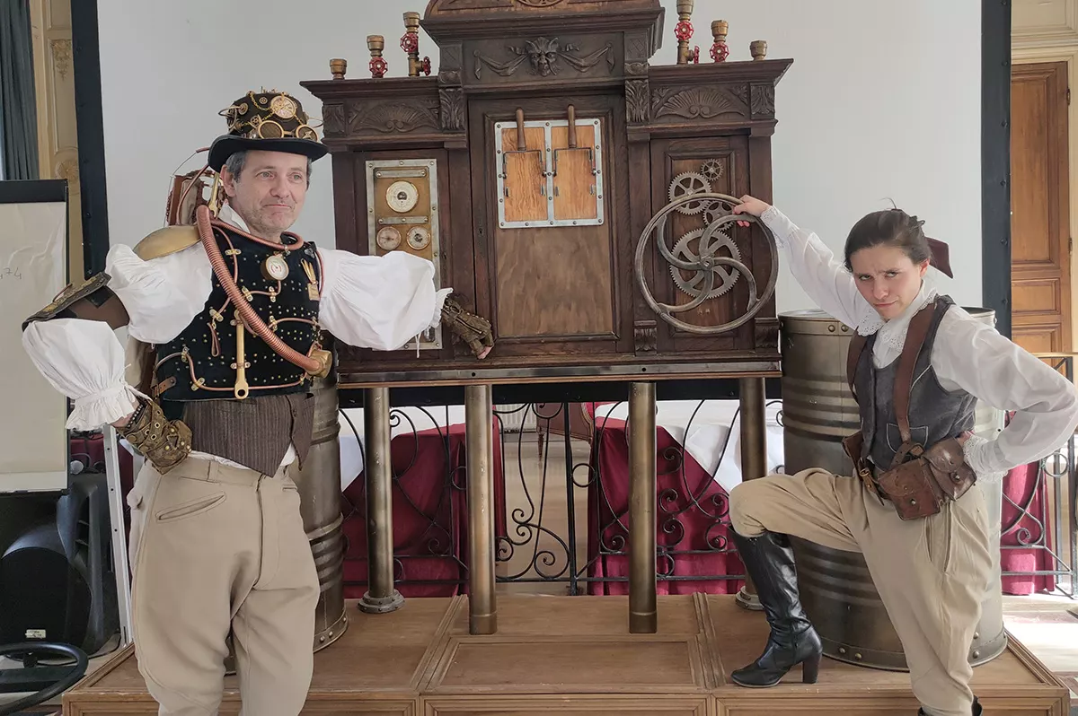 Deux comédiens en costume steampunk devant un meuble à engrenages